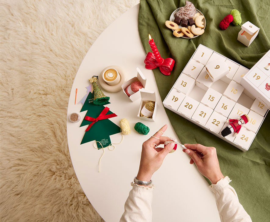 Ricorumi Adventskalender liegt geöffnet auf einem Tisch und Person häkelt.