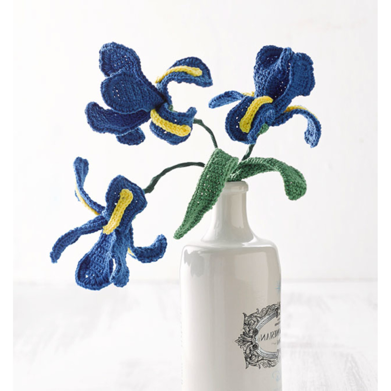 Häkeln so bunt wie die Natur: Handgefertigte blaue und gelbe Häkelblumen in weißer Vase.