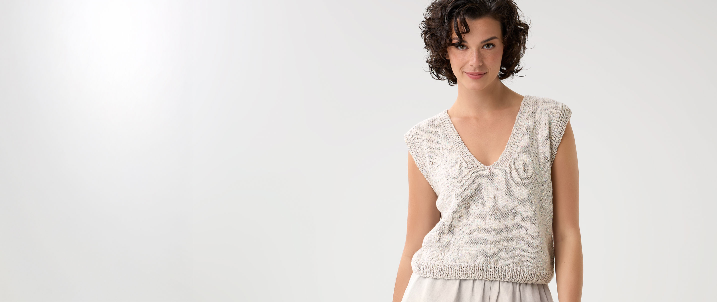 Model trägt beigefarbenes Stricktop mit V-Ausschnitt vor einem hellen Hintergrund.