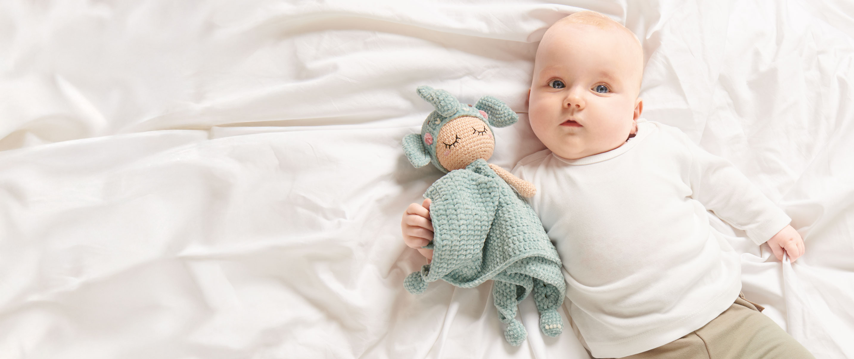 Ein liegendes Baby hält ein gehäkeltes Schnuffeltuch in Elefanten-Design im Arm. 