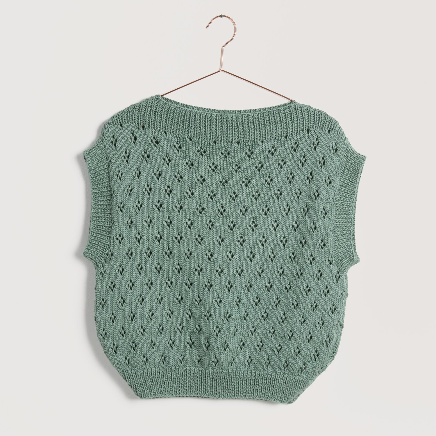 Lovewool No. 22 Frühjahr-Sommer: Grüner Strickpullover mit Lochmuster, hängend an einem Kleiderbügel.