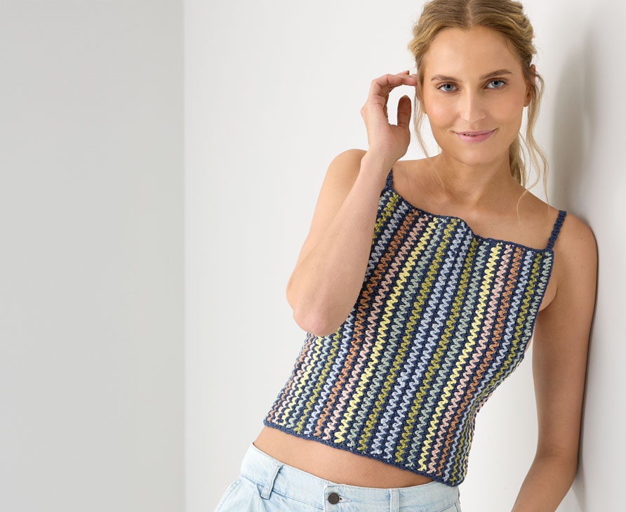 Frau mit buntem Häkeltop lehnt an einer Wand.