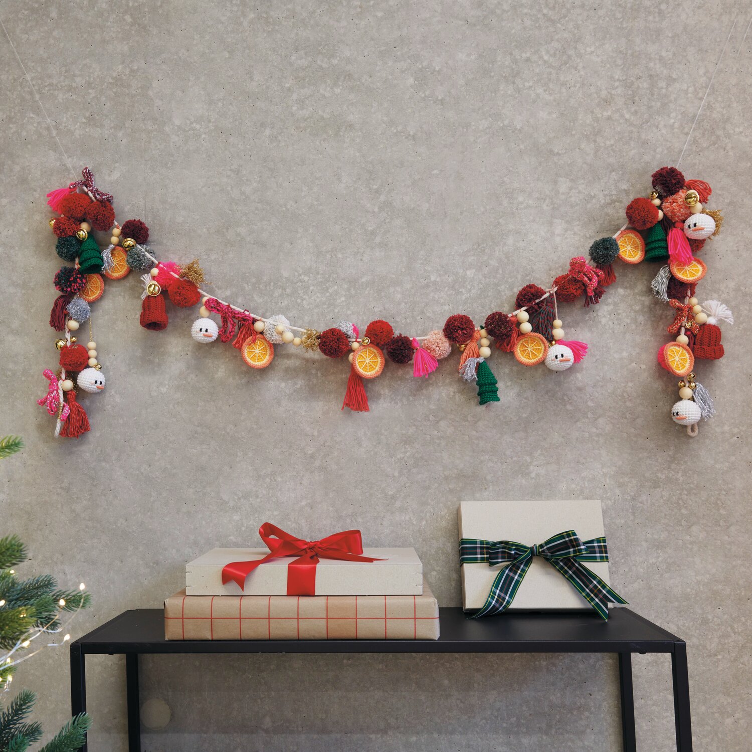 Ricorumi DIY Adventskalender: Bunte Girlande mit Pompons und Figuren, dekorativ über Geschenken an der Wand hängend.