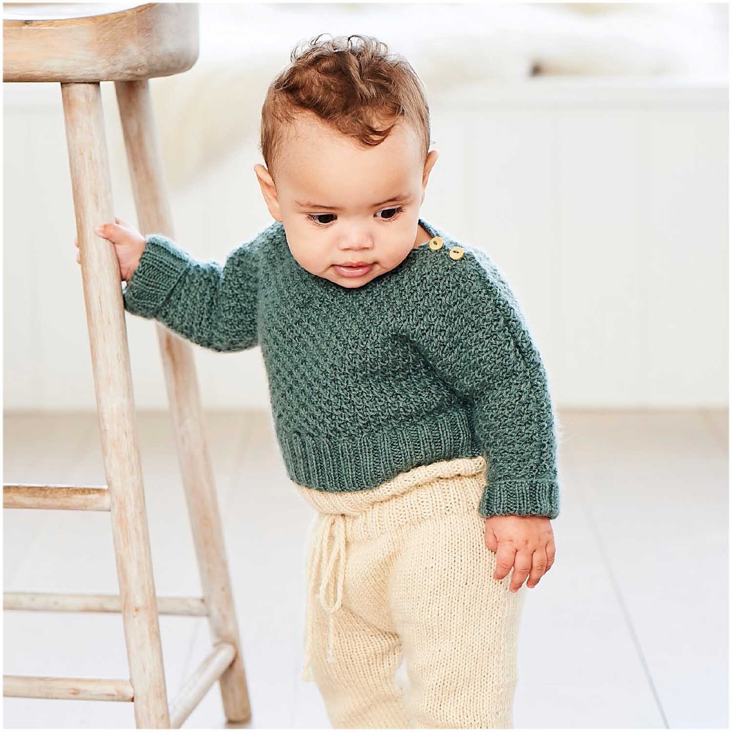 Rico Baby Dream dk uni - A Luxury Touch: Ein Baby trägt einen gestrickten Pullover in Efeu von Rico Design.