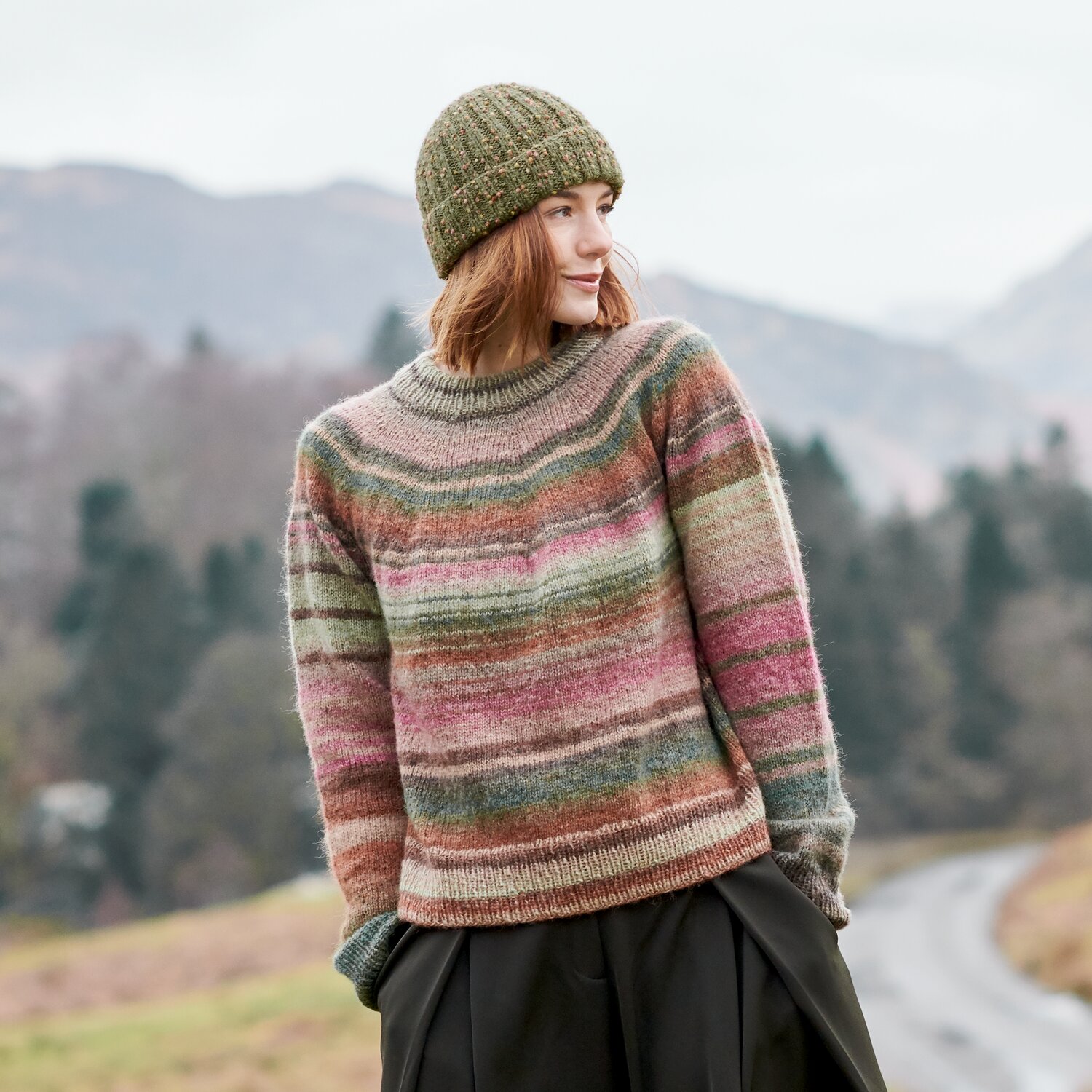 Strickset Pullover Modell 27 aus Lovewool No. 23, lässiger Damen-Pullover mit mehrfarbigen Querstreifen und passender Mütze, getragen in herbstlicher Landschaft