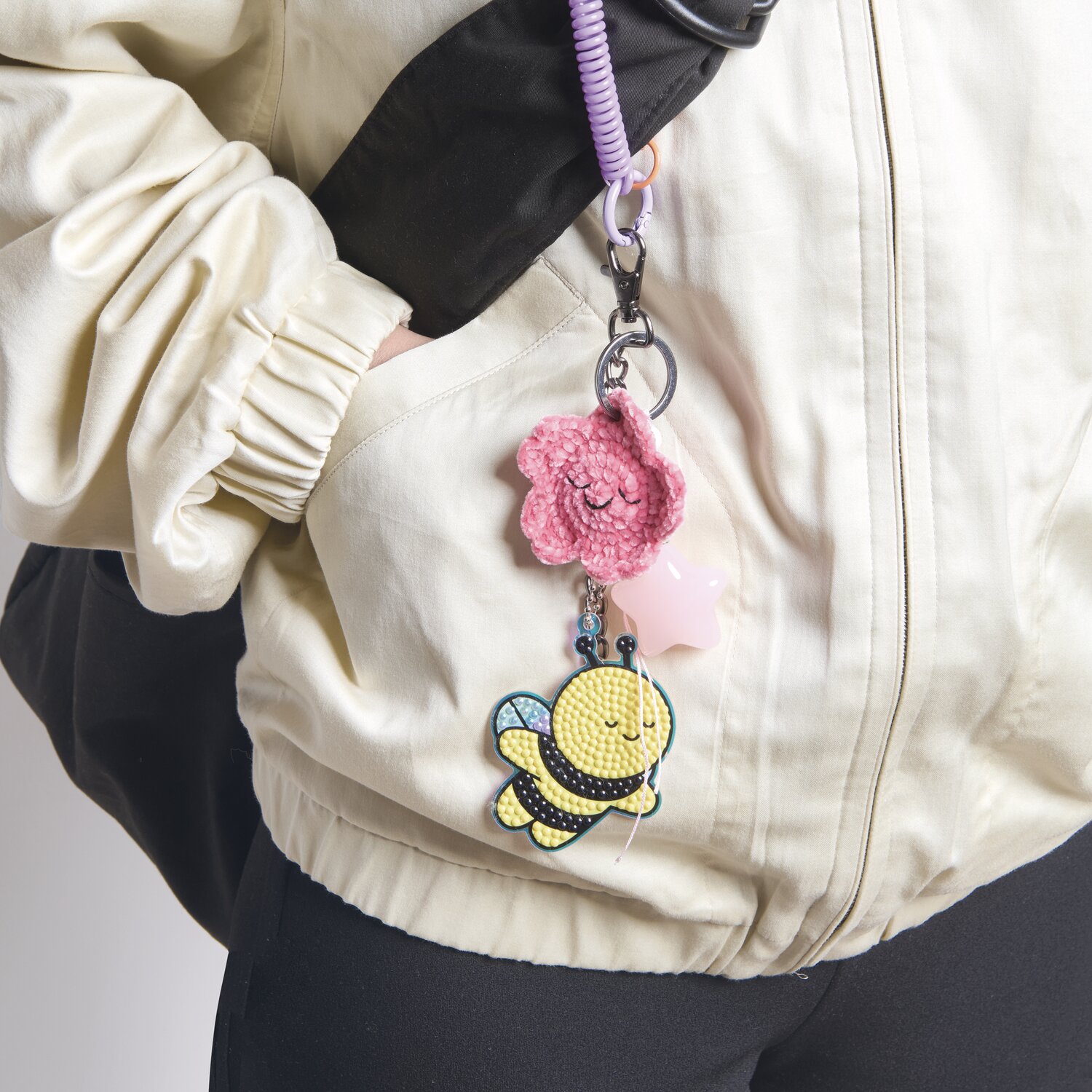 Ricorumi Rico Chingus Schlüsselanhänger mit rosa Blume und Biene an weißer Jacke befestigt.