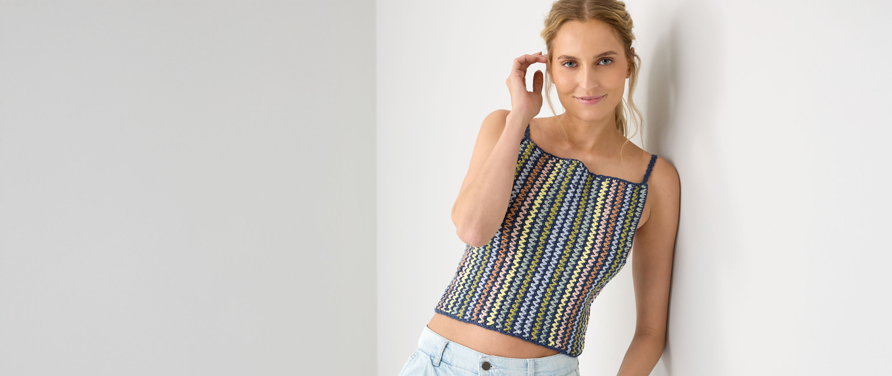 Frau mit buntem Häkeltop lehnt an einer Wand.