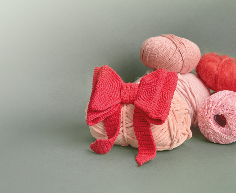 8 rosafarbene und rote Wollknäuel mir roter Häkel-Schleife