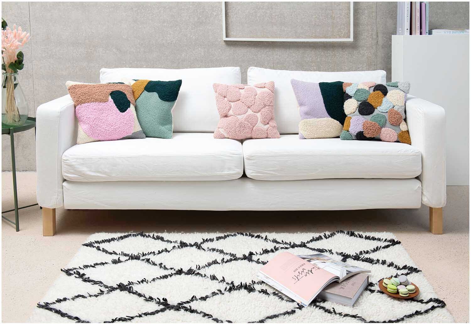 Punch Needle Packung Kissen Punkte bunt auf weißem Sofa, dekoriert mit farbenfrohen Kissen von Rico Design.