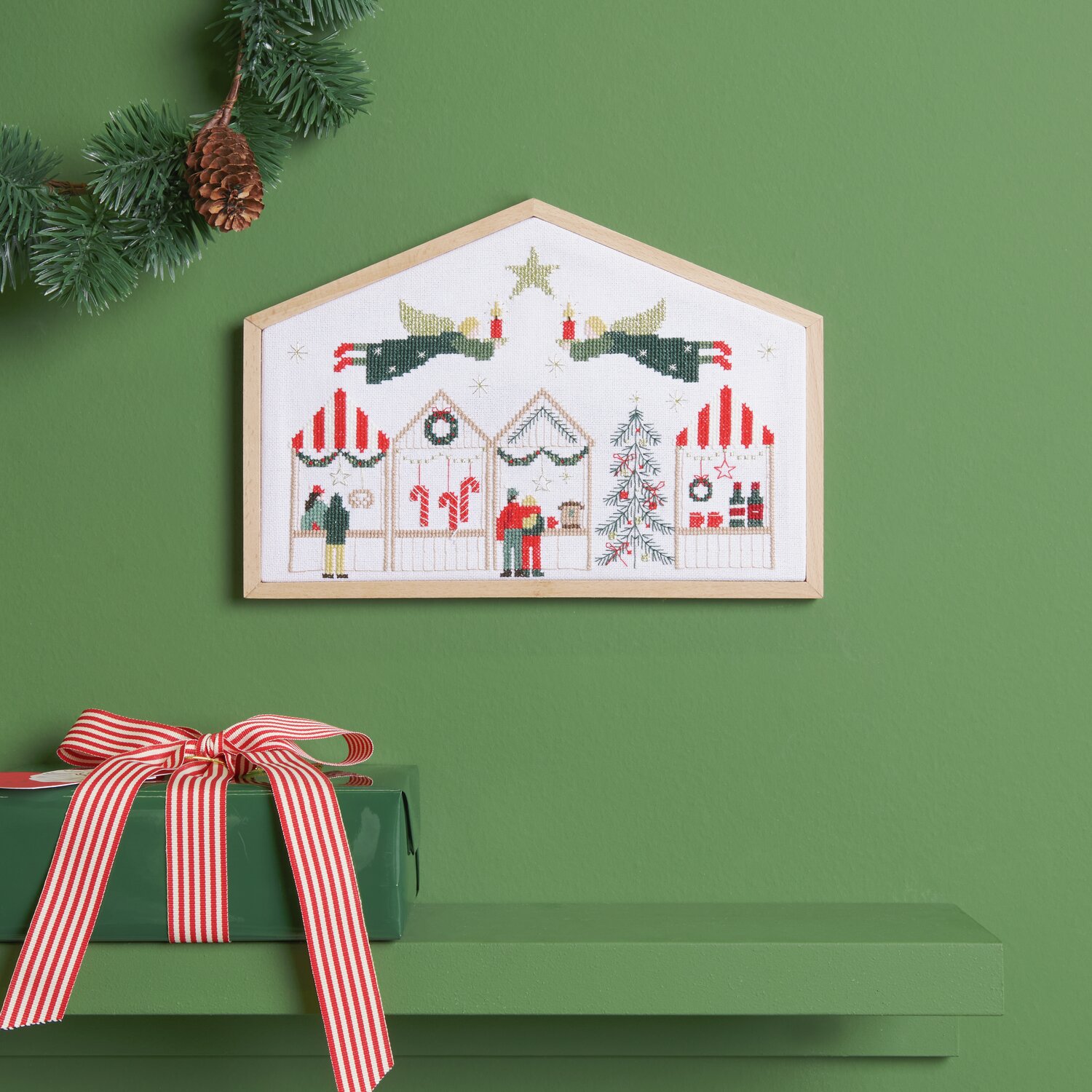 Stickpackung Weihnachtsmarkt 27,5x19cm von Rico Design Stickpackung Weihnachtsmarkt zeigt ein festliches Motiv mit Weihnachtsbuden und Tannenbaum, eingerahmt an einer grünen Wand.