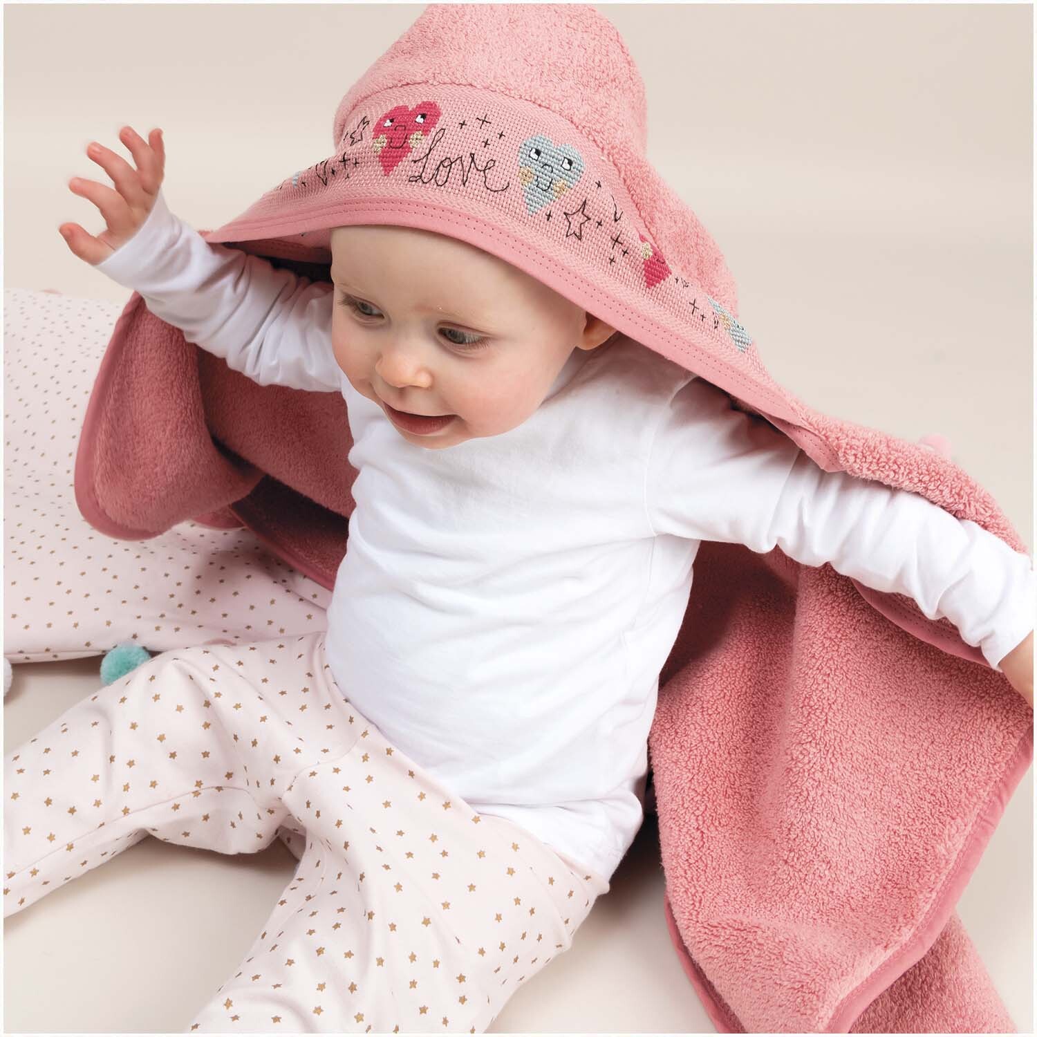 Badetuch mit Kapuze 80x70cm in Hellpink von Rico Design, zeigt ein Baby, das in das weiche Handtuch gehüllt ist.