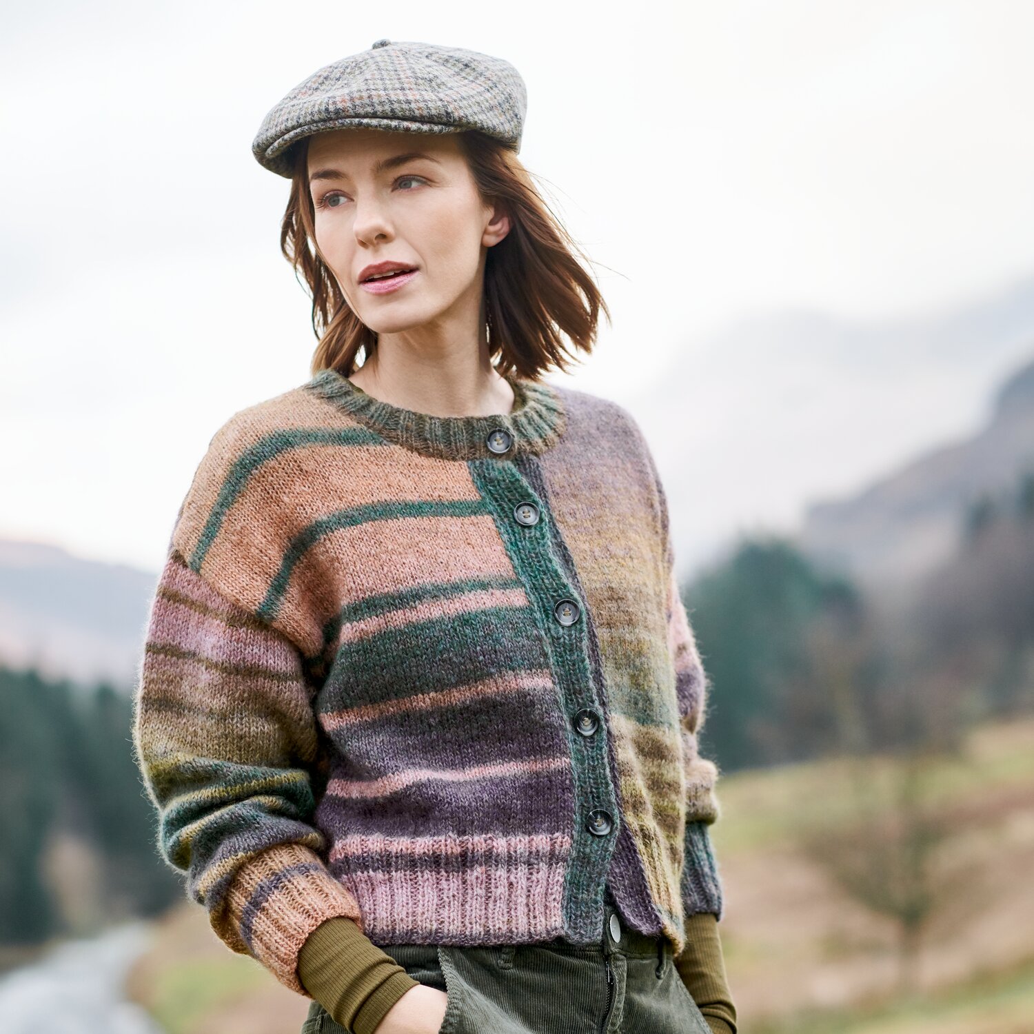 Strickset Jacke Modell 24 aus Lovewool No. 23, gestreifte Damenstrickjacke mit Knopfleiste, kombiniert mit Schirmmütze und Hose in herbstlicher Landschaft