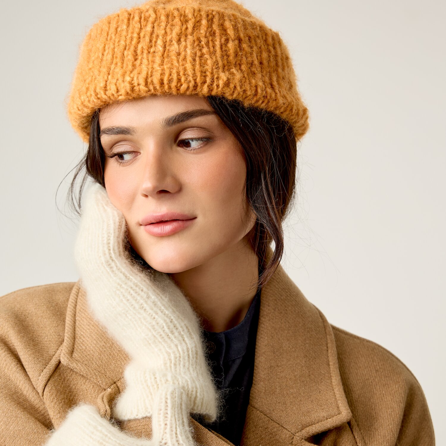 Strickset Fäustlinge Modell 12 aus Luxury Knits Little Pieces, weiche lang geschnittene Wollfäustlinge in Naturweiß, getragen von Frau im Wollmantel mit Strickmütze