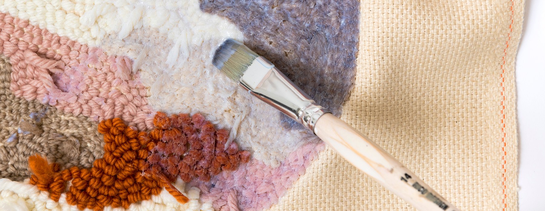 Pinsel streicht Kleber auf Rückseite von einem Punch Needle Stickbild