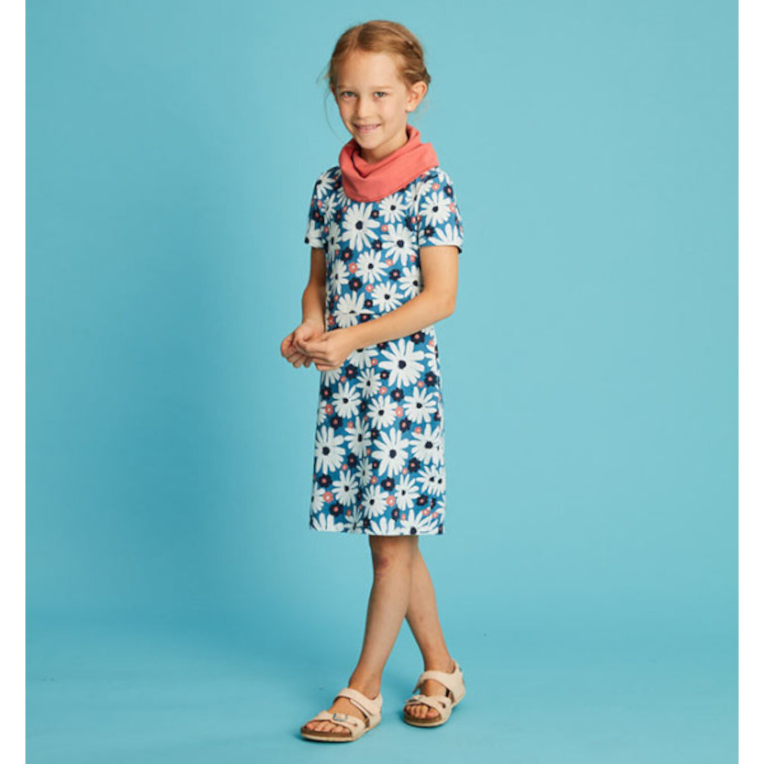 Der Jersey Kleiderbaukasten für Kids: Mädchen in geblümtem Kleid mit rosa Schal vor blauem Hintergrund.