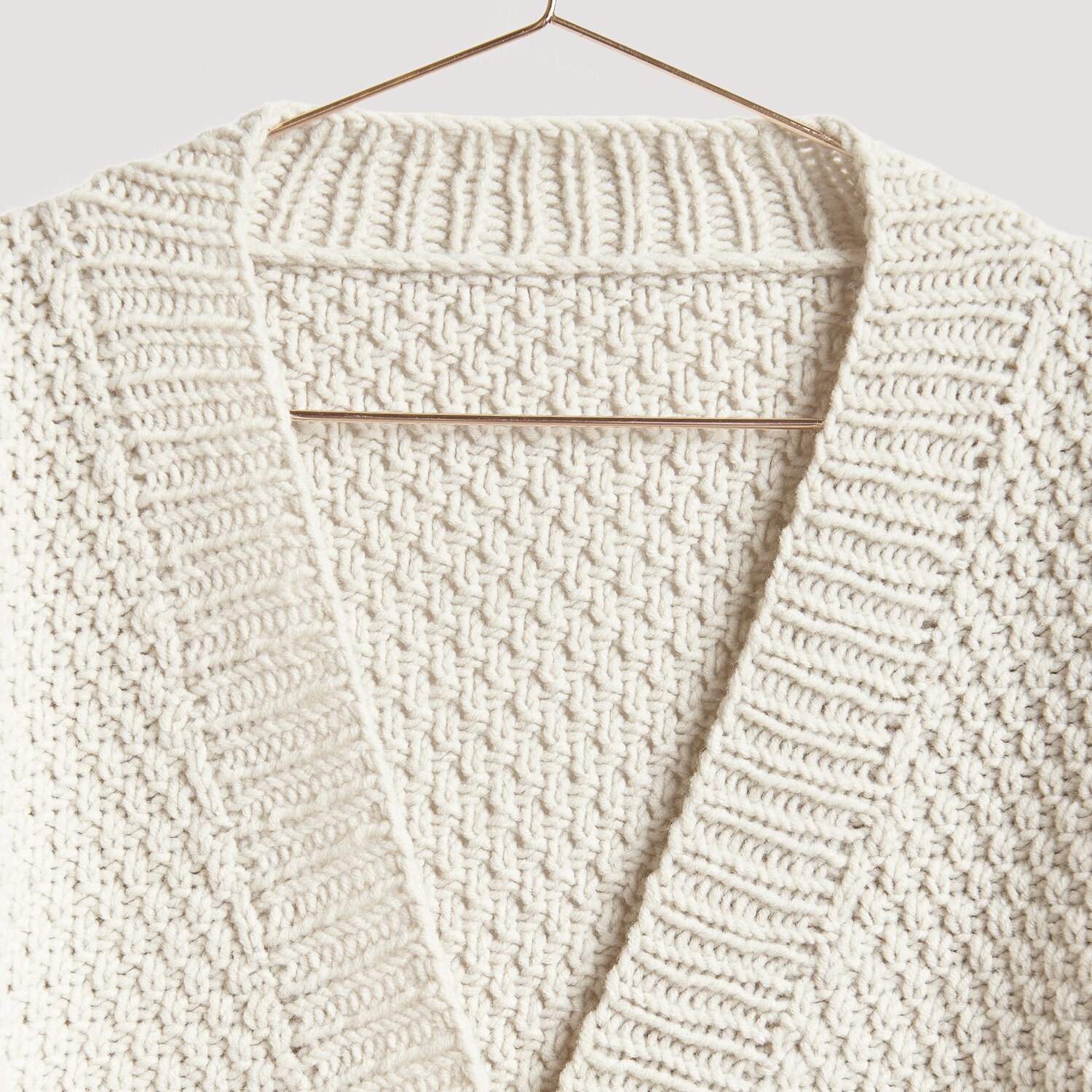 Die Neue Masche No. 13 Herbst: Cremefarbener Strickpullover mit Zopfmuster, präsentiert auf einem Kleiderbügel.