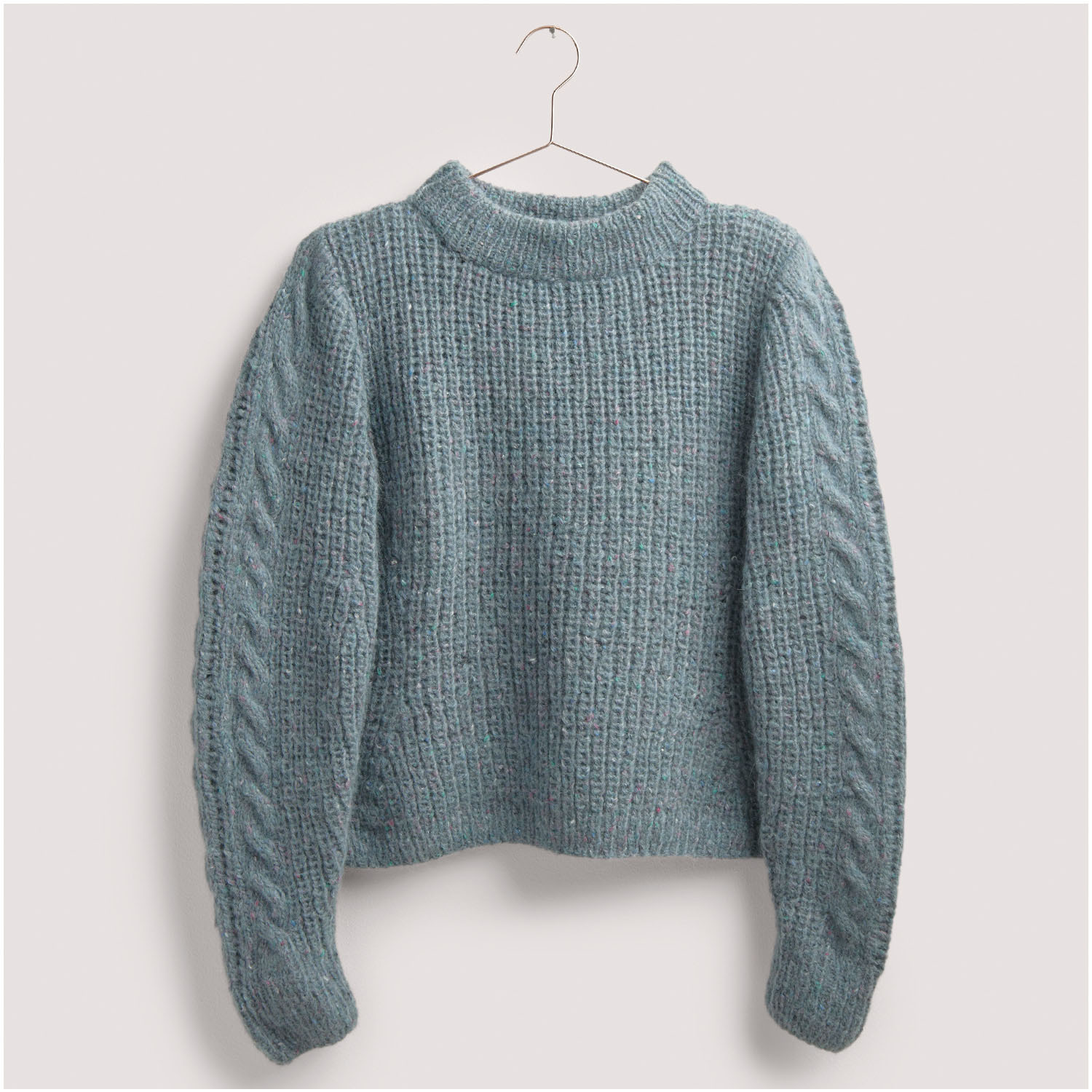 Strickset Pullover Modell 24 aus Die Neue Masche Nr. 8: Hellblauer Pullover mit Zopfmusterärmeln auf einem Kleiderbügel.