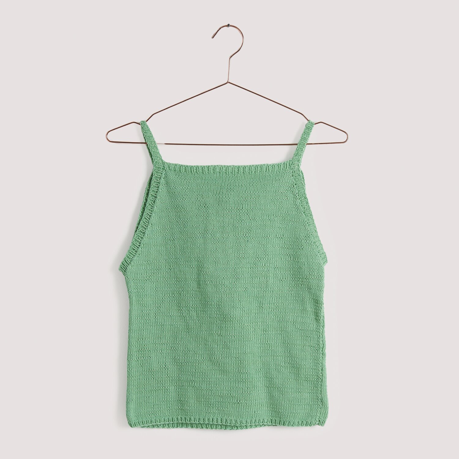 Strickset Top Modell 24 aus Die Neue Masche No. 15: Grünes, ärmelloses Stricktop auf einem Kleiderbügel vor neutralem Hintergrund.
