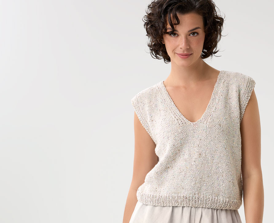 Model trägt beigefarbenes Stricktop mit V-Ausschnitt vor einem hellen Hintergrund.
