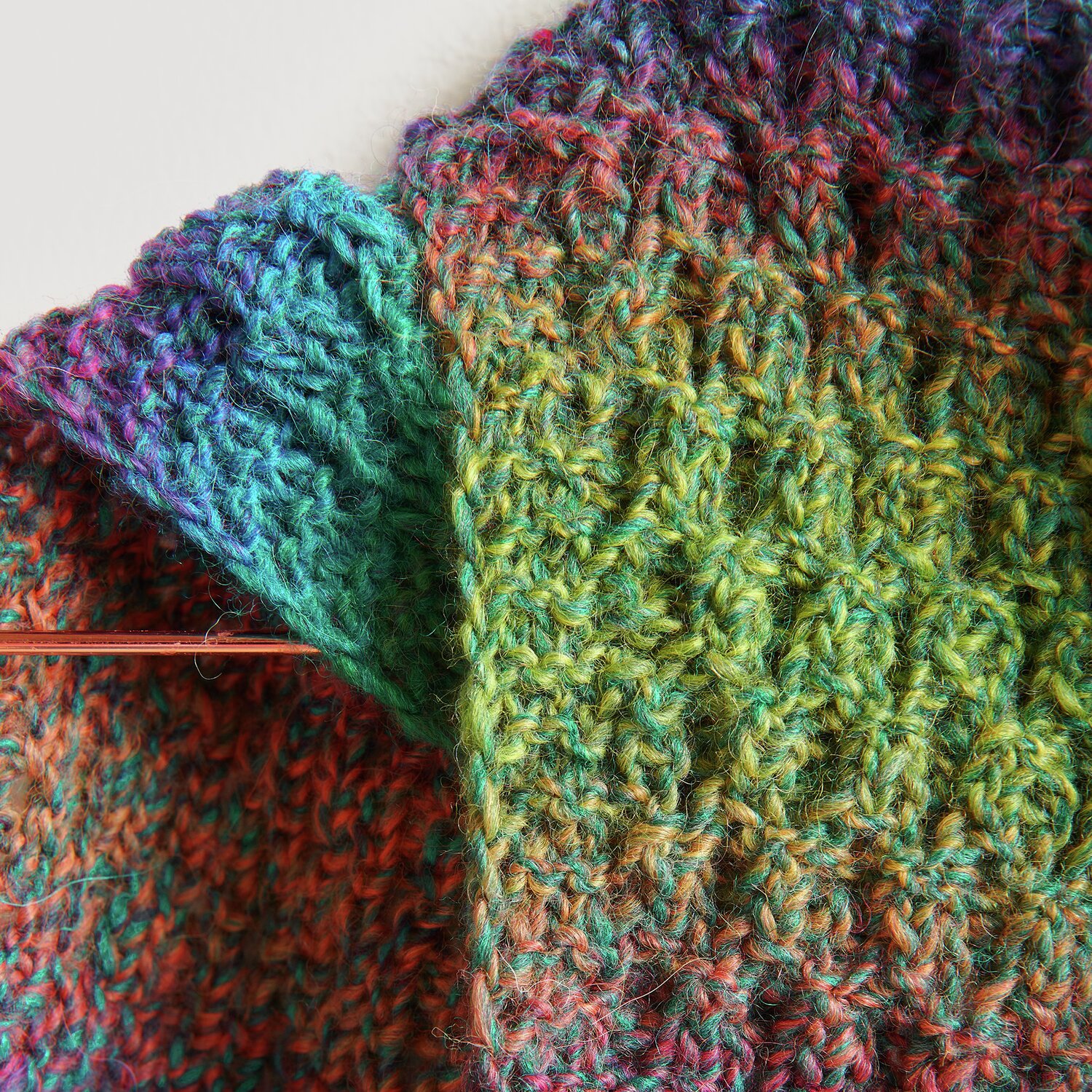 Creative Melange Alpaca Wonderball dk zeigt ein gestricktes, buntes Textil mit Stricknadel.