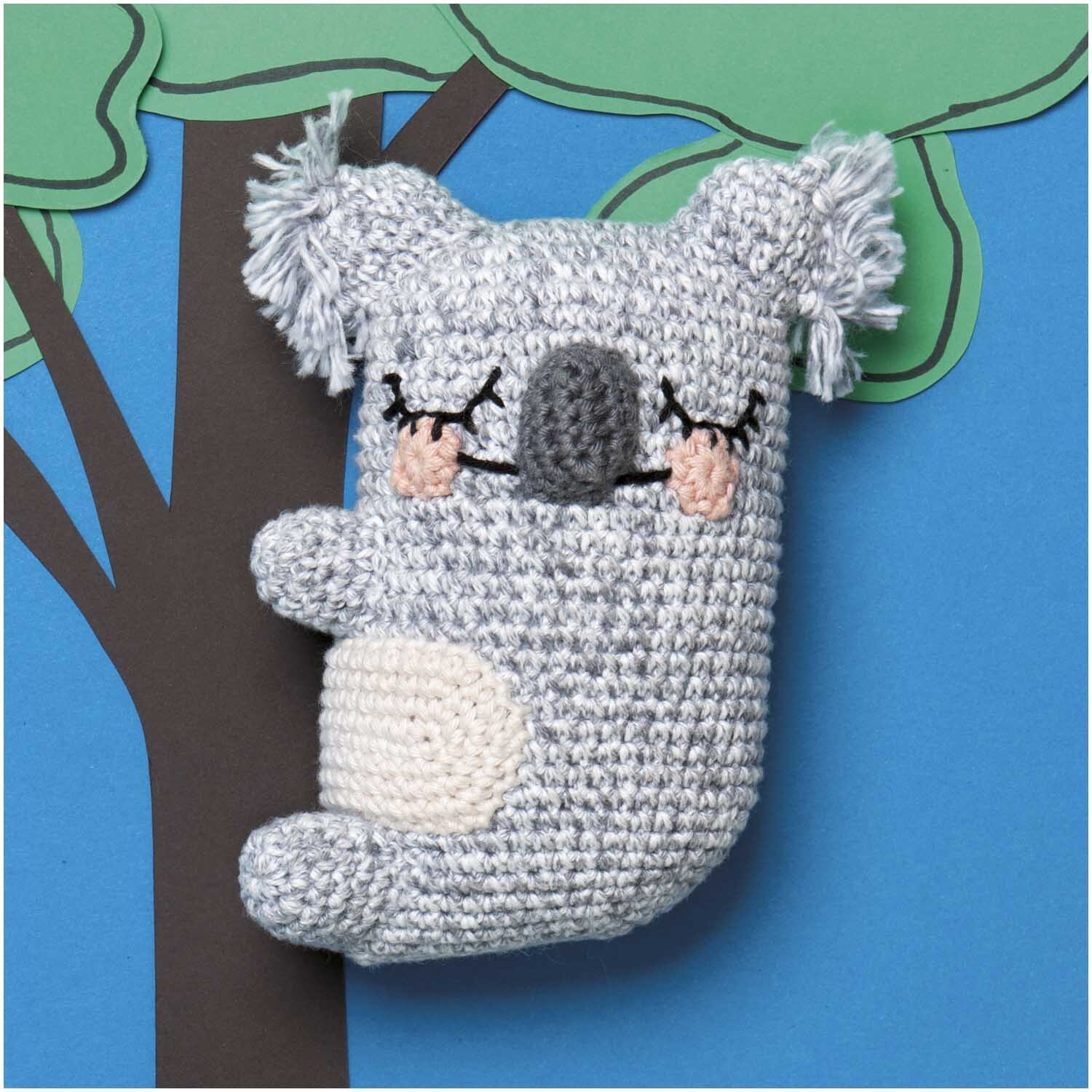 Creative Ricorumi Spray dk: Ein gehäkelter Koala in Grau hängt an einem Baum vor blauem Hintergrund.