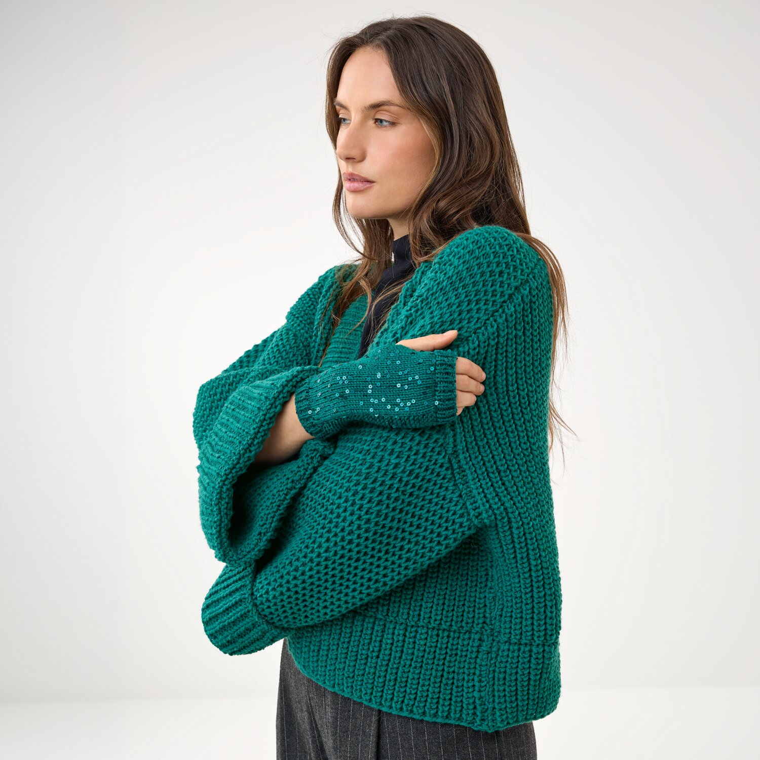 Strickset Stulpen Modell 13 aus Die Neue Masche No. 16, gestrickte Handstulpen an Frau mit passendem, grob gestricktem Pullover in modernem, minimalistischen Studio.