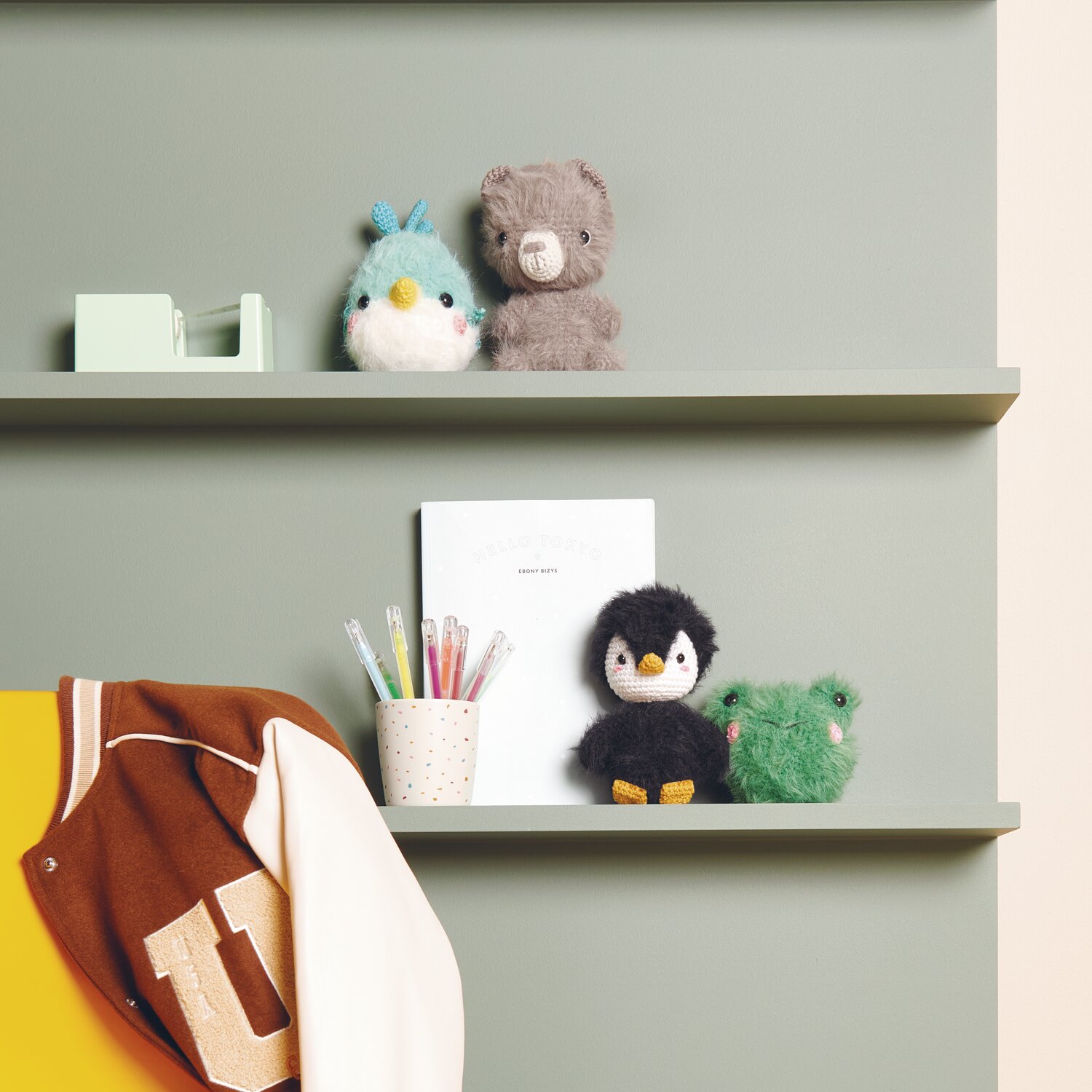 Creative Ricorumi dk 25g Farbe Senf von Rico Design Ricorumi Furry Animals auf einem Regal mit Stiften und Jacke. Farben: Türkis, Schwarz, Grün.