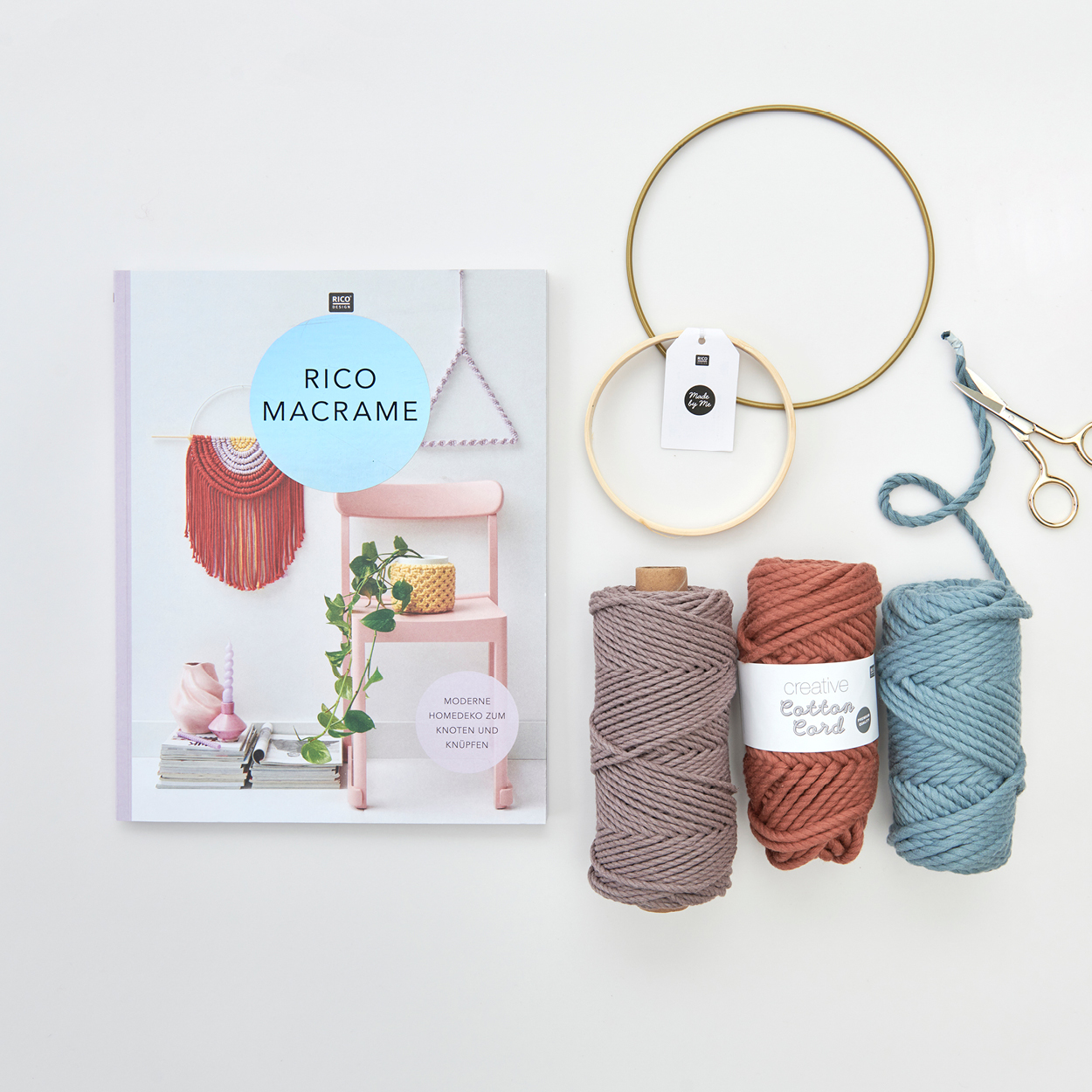 Rico Macrame Anleitungsheft mit drei Kordel-Garnen in verschiedenen Farben, zwei unterschiedlich Große Metallringe und eine Schere. Flatlay von Produkten.