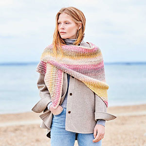 Frau trägt gestricktes Dreieckstuch, im Hintergrund Meer