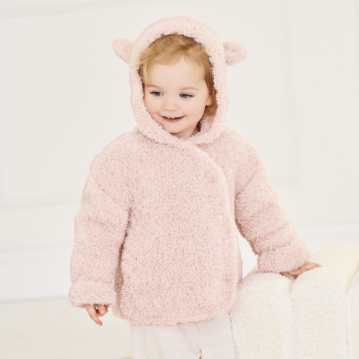 Strickanleitung Babyjacke aus Creative Teddy: Flauschige rosa Jacke mit Kapuze und Ohren, ideal für Babys.