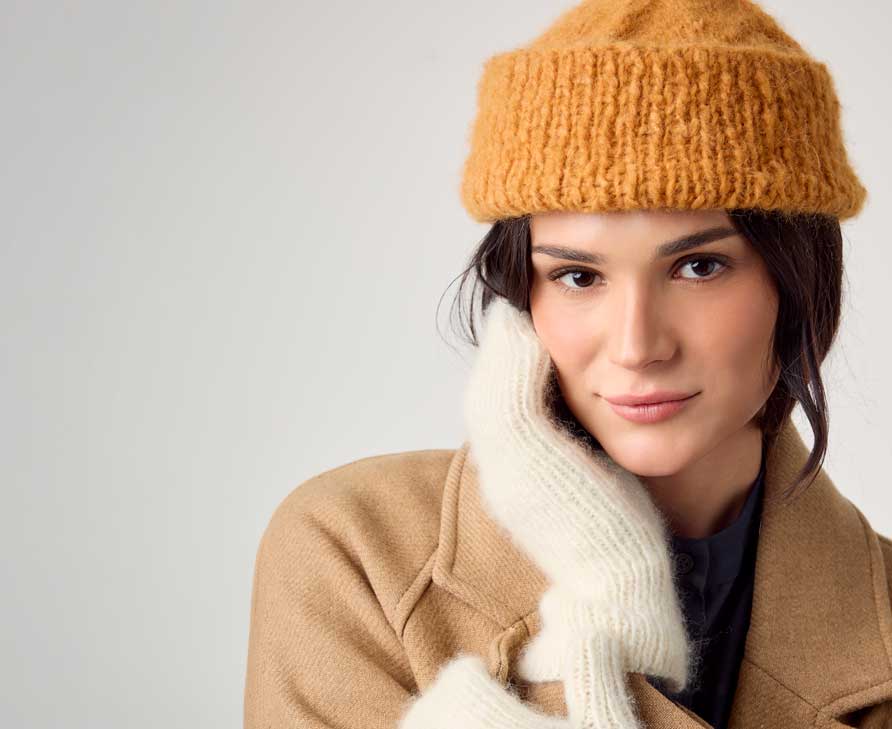 Frau trägt senffarbene Strickmütze und cremefarbene Strickhandschuhe