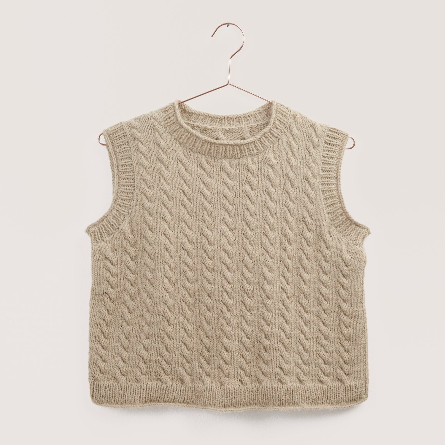 Strickset Top Modell 08 einfädig aus Made by Me Nr. 18, beige, mit Zopfmuster, hängt an einem Kleiderbügel.