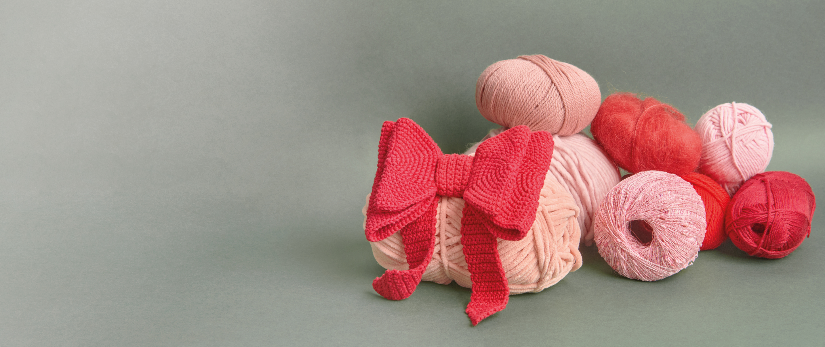 8 rosafarbene und rote Wollknäuel mir roter Häkel-Schleife