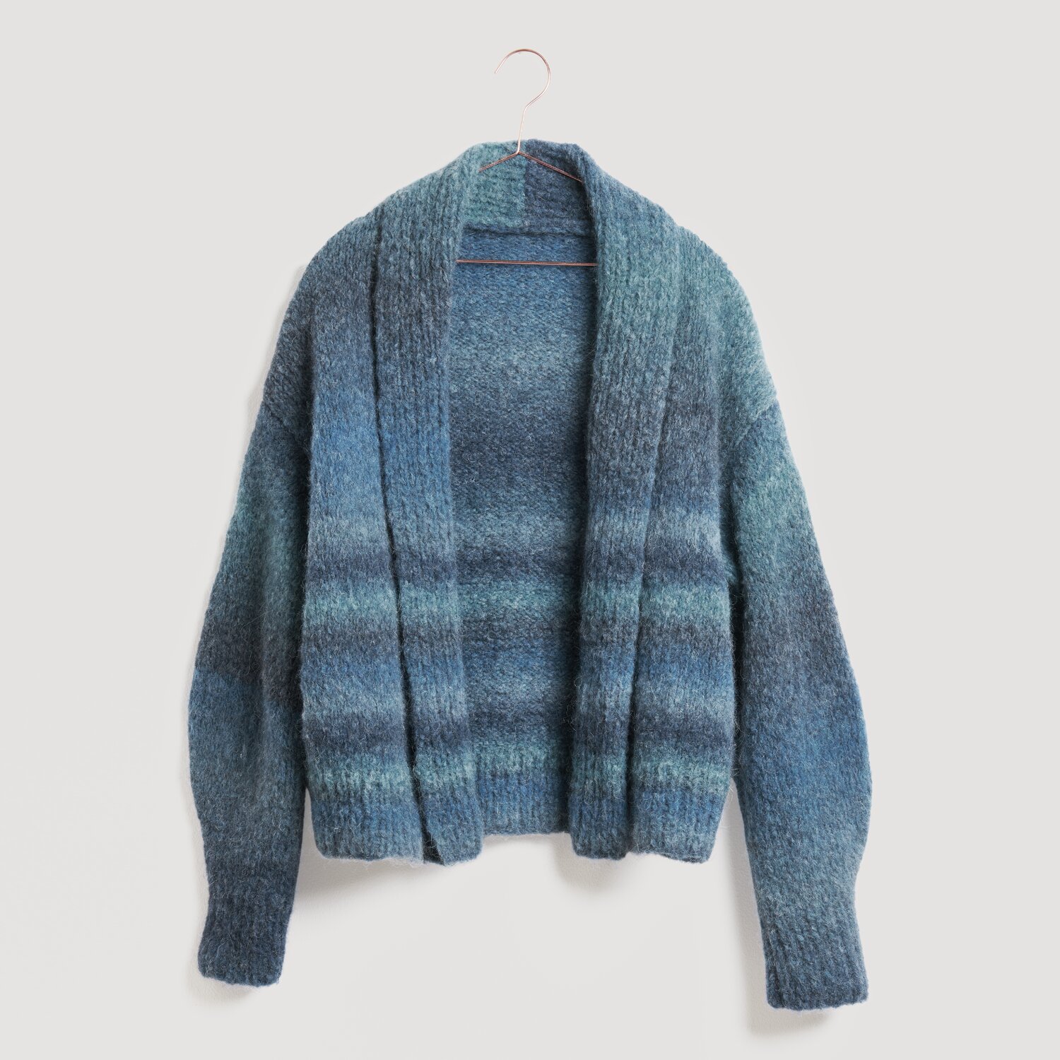 Blauer Strickpullover von Modell Legeware, hängend an einem Kleiderbügel. Der Pullover zeigt ein gestreiftes Muster in verschiedenen Blautönen und hat lange Ärmel. Ideal für kühle Tage.