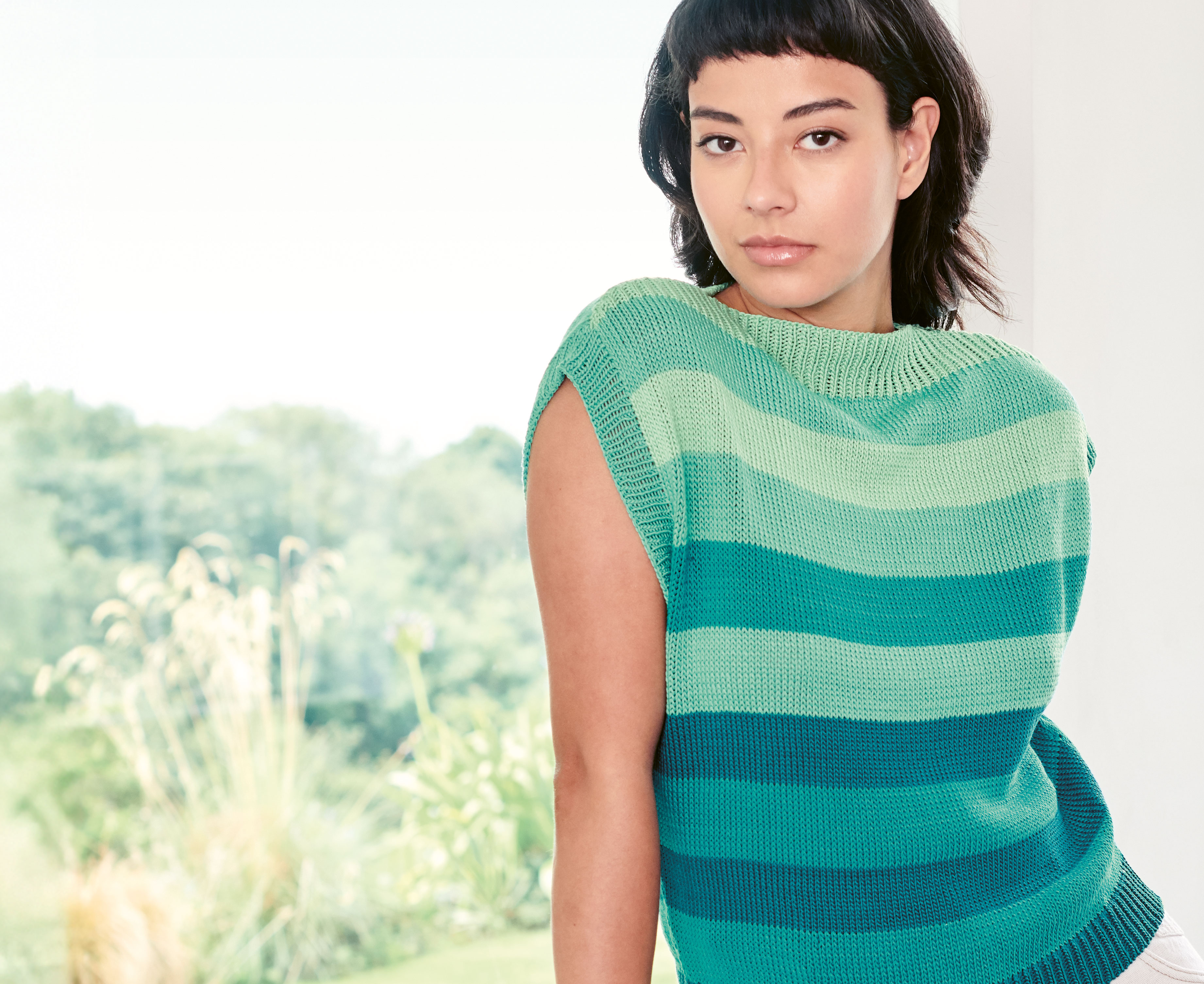 Stricktop in Aquatönen mit Blockstreifen wird von einem Model getragen vor einer Meeres-Kulisse.