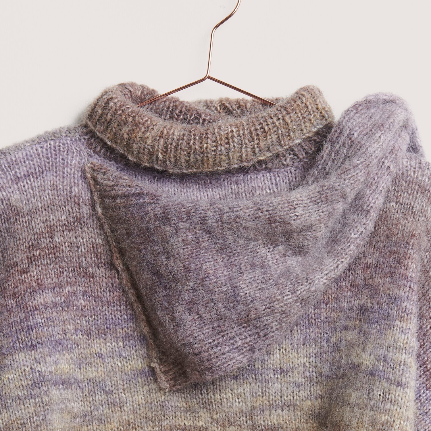 Die Neue Masche No. 14 Winter von idee. Creativmarkt Creative Painted Power: Strickpullover in sanften Herbsttönen, aus weicher Wolle, auf einem Kleiderbügel.