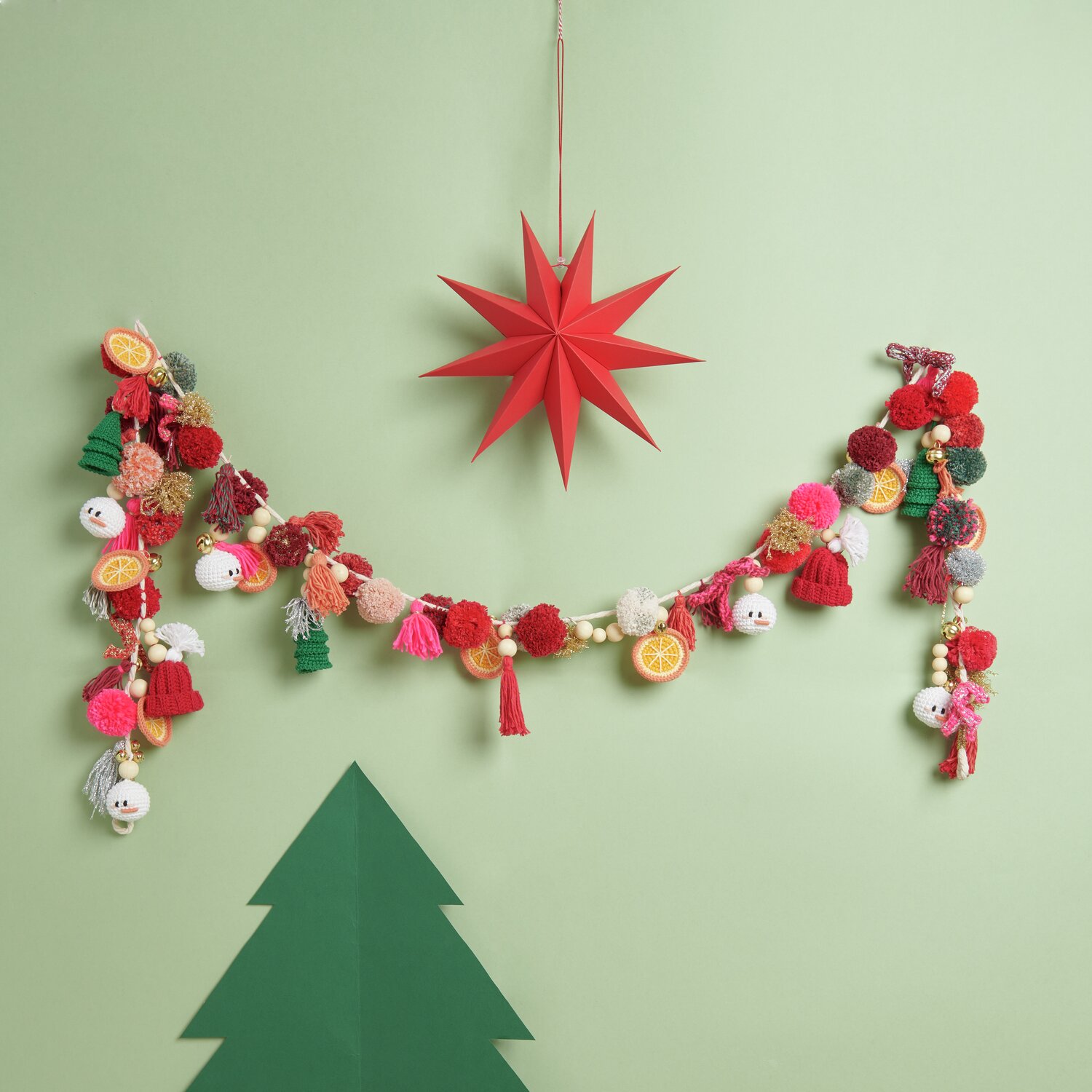 Ricorumi DIY Adventskalender: Bunte Girlande mit Pompons und Anhängern vor grünem Hintergrund.