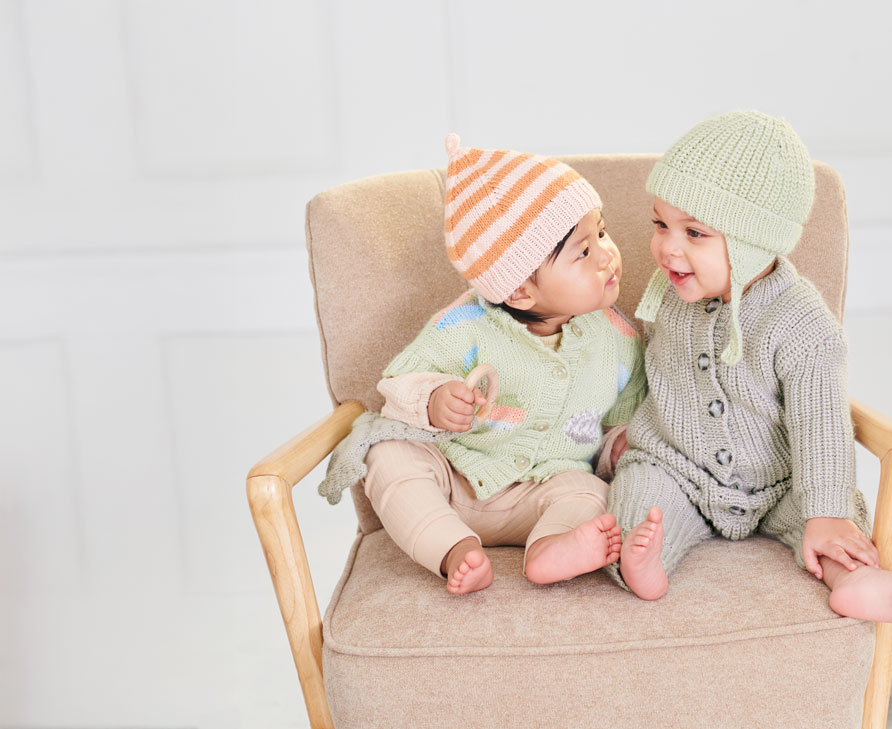 Baby in Strickjacken und Strickmützen sitzen auf einem Sessel