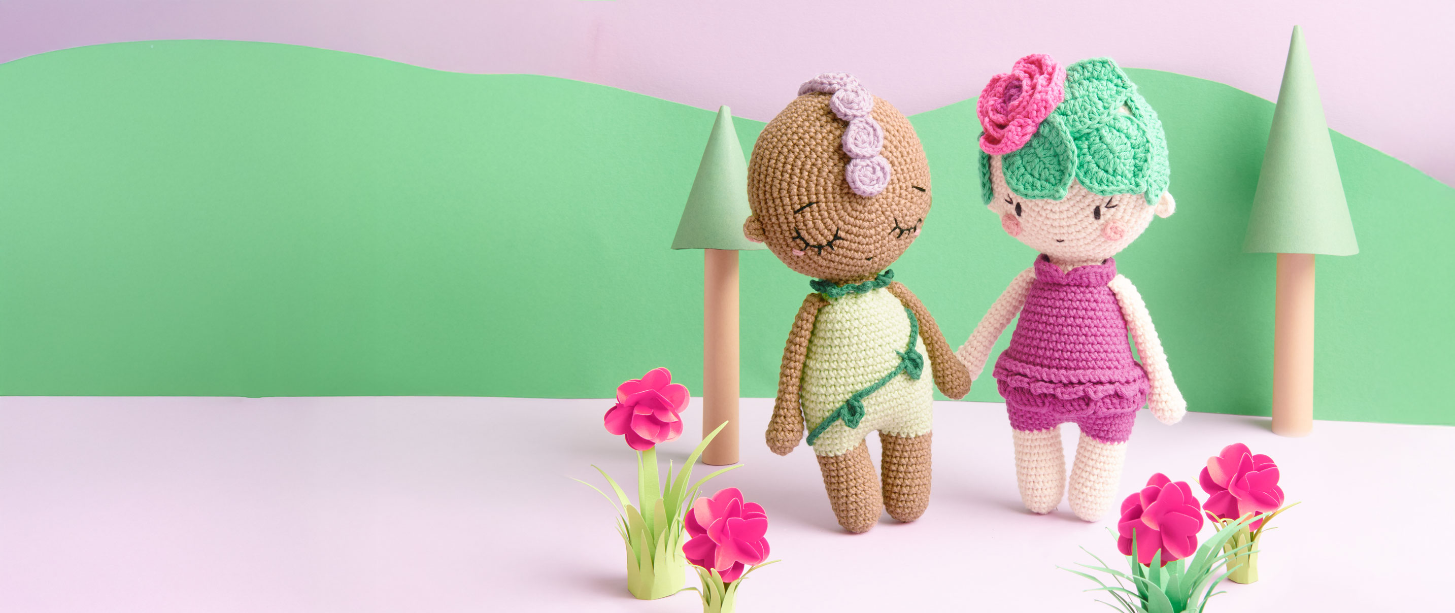 Ricorumi Häkelfiguren in Form von Blumen stehen vor gebasteltem Hintergrund und halten Händchen.