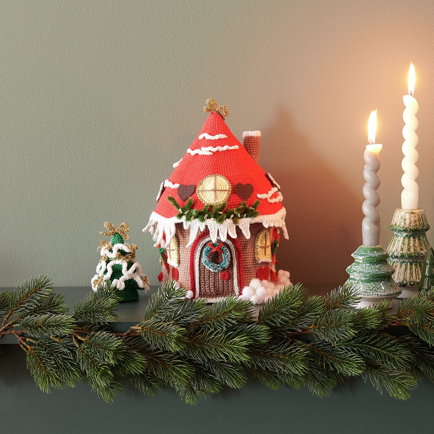 Ricorumi Adventskalender: Weihnachtliches Häuschen in Rot mit Kerzen und Tannenzweigen dekoriert.