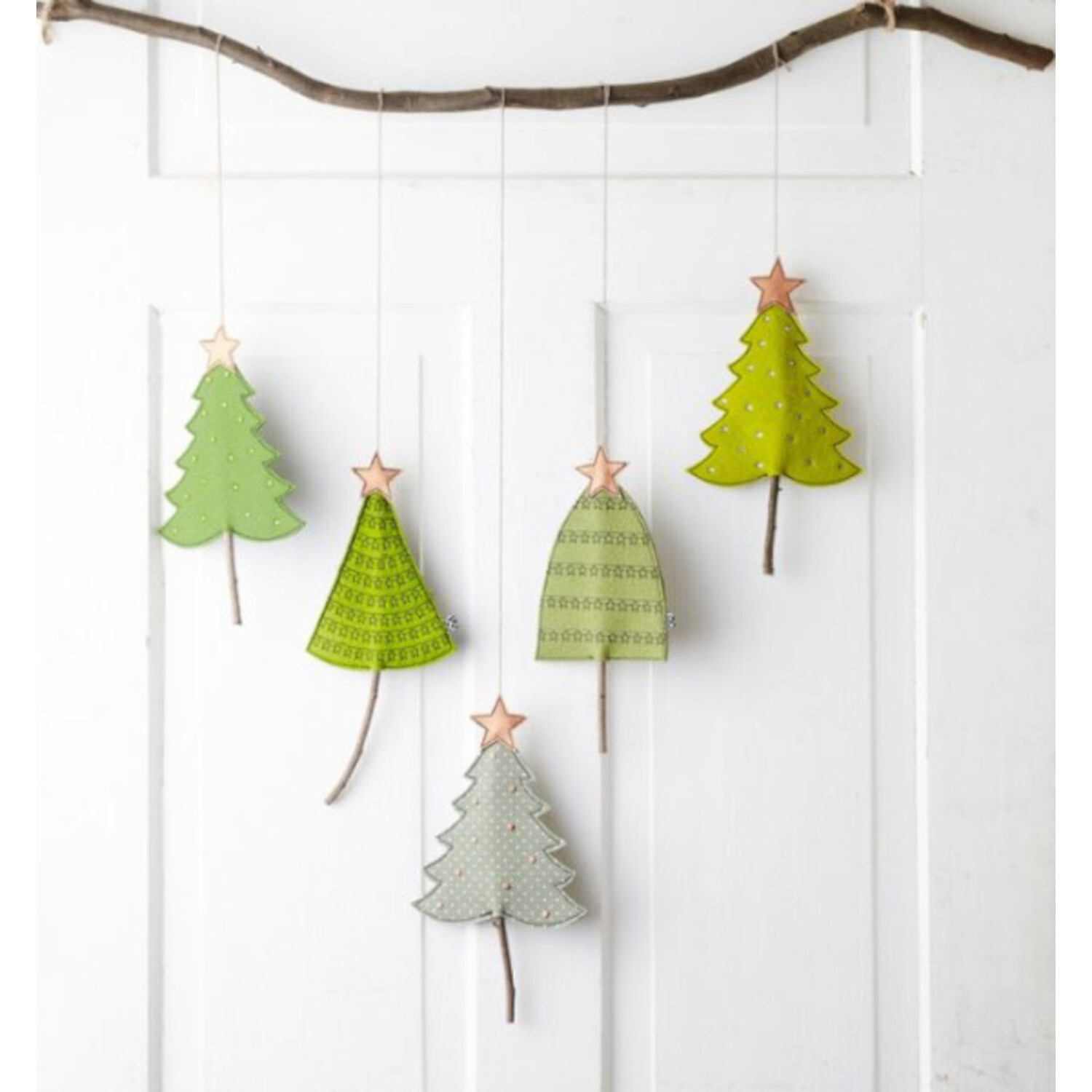 Winterdeko Nähen im Skandi-Stil: Fünf grüne und gelbe Stofftannen hängen an einem Ast vor weißer Tür.
