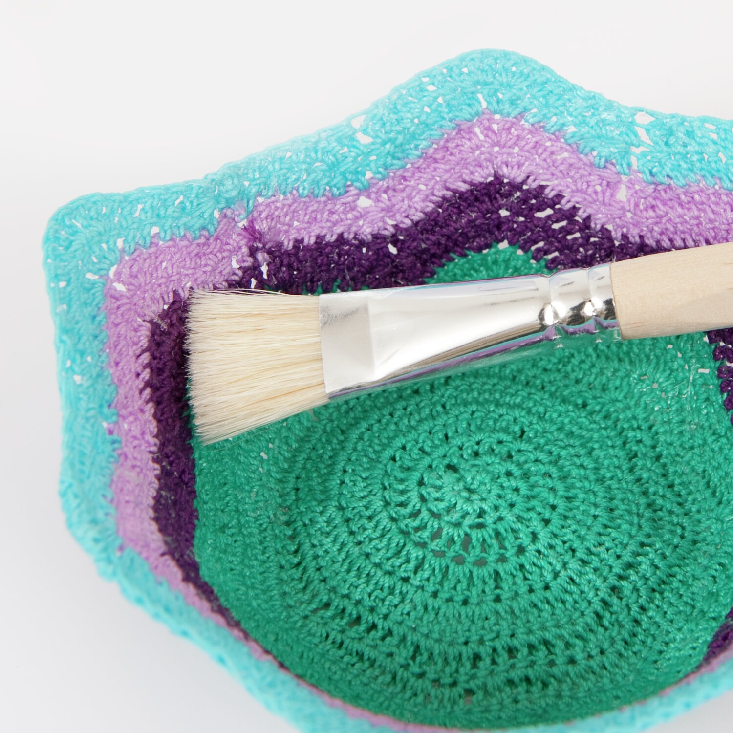 Textilsteif  105g von Rico Design Textilsteif, Pinsel auf gehäkeltem Untergrund in Türkis, Lila und Grün, ideal für kreative Projekte.