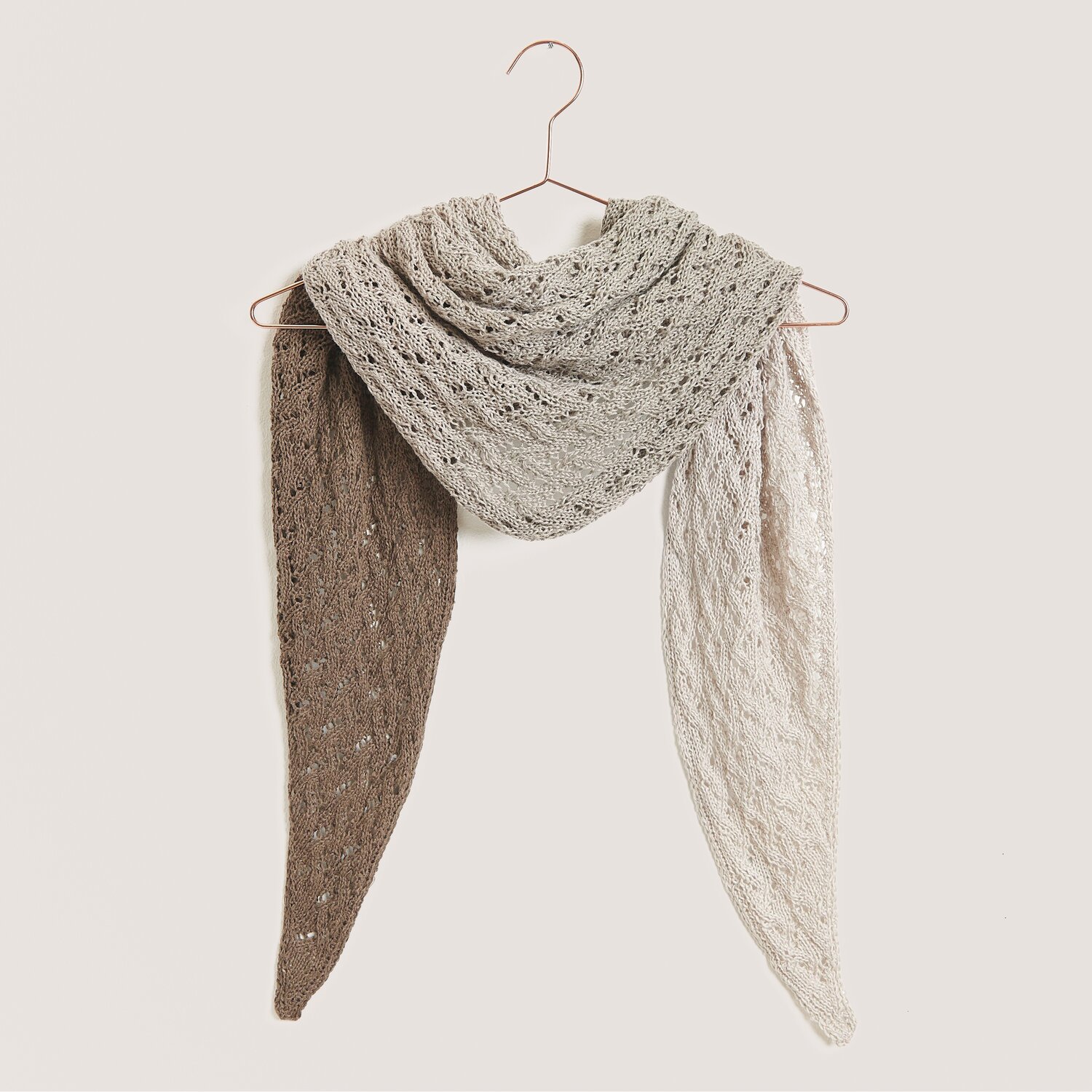 Strickset Dreieckstuch Modell 03 aus Tücher Special von Rico Design Strickset Dreieckstuch Modell 03 aus Tücher Special in Naturtönen, gehäkelt aus Creative Cotton Dégradé Lucky 8, hängt auf einem Kleiderbügel.