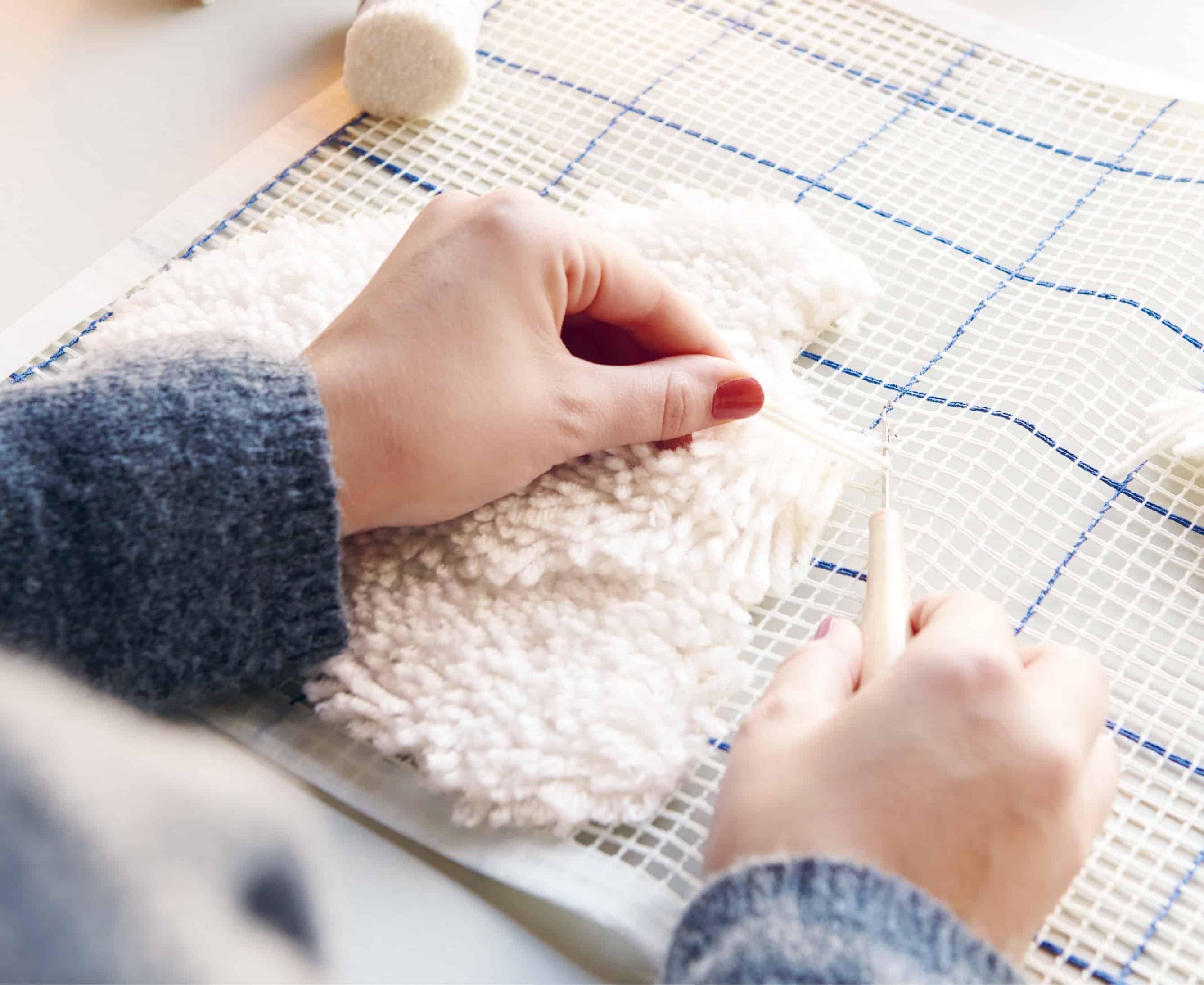 Hände knüpfen mit Hilfe eines Knüpfhakens weißes Garn an Stramin fest