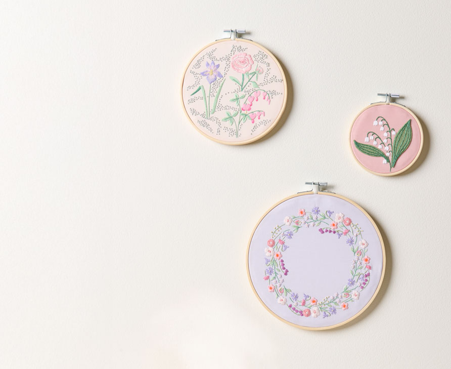 3 Stickringe mit Blumenstickbildern hängen an einer Wand