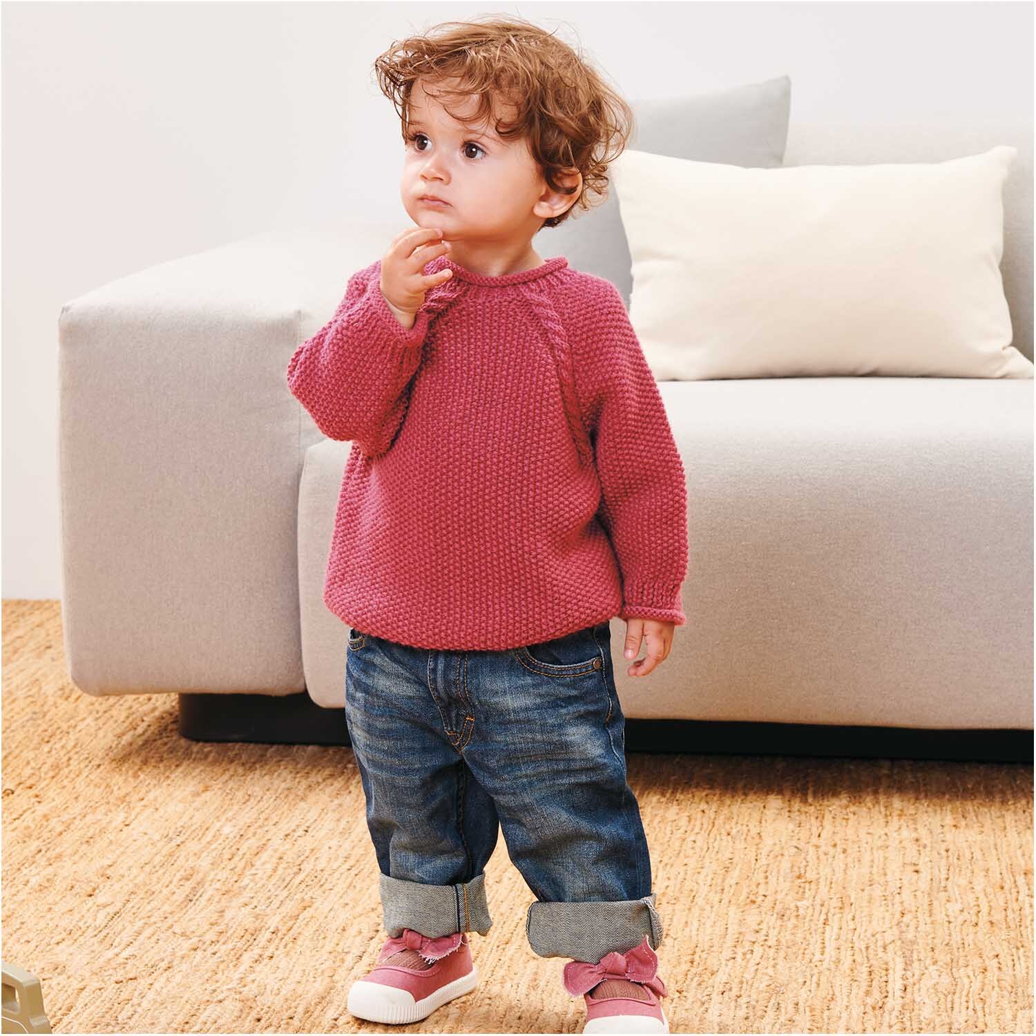 Rico Baby Dream dk uni - A Luxury Touch: Kleinkind im bordeauxfarbenen Pullover von Rico Design, stehend vor einem Sofa.