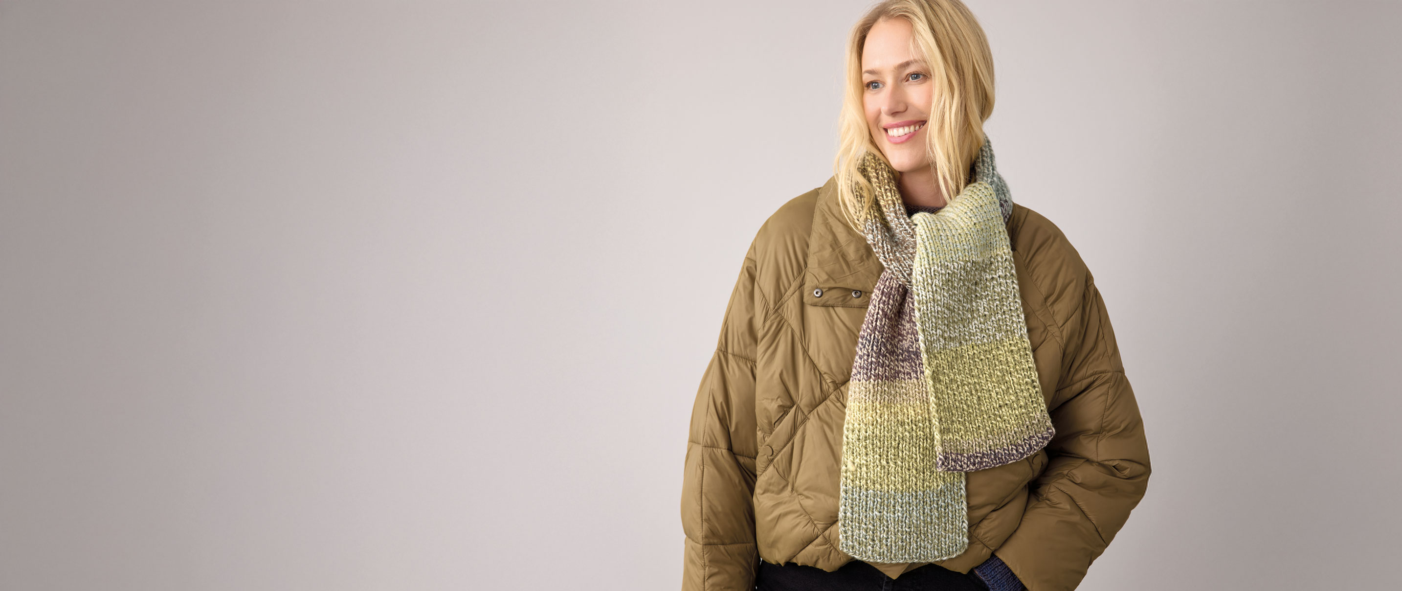 Frau trägt grünen Strickschal vpr hellem Hintergrund