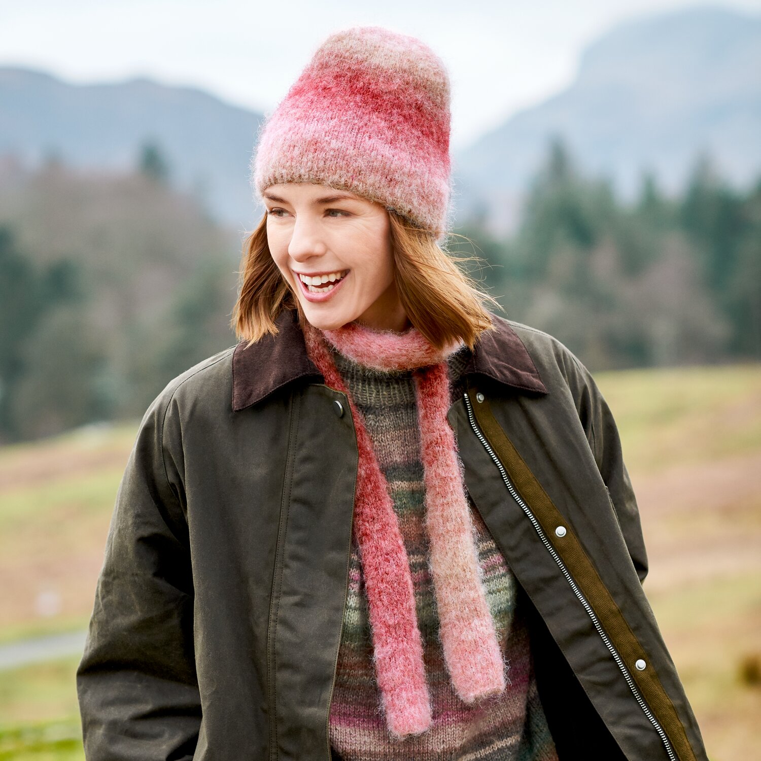 Strickset Mütze + Schal Modell 29+30 aus Lovewool No. 23, Frau im Freien mit weich verlaufendem rosa Strickaccessoire, kombiniert mit dunkler Outdoorjacke