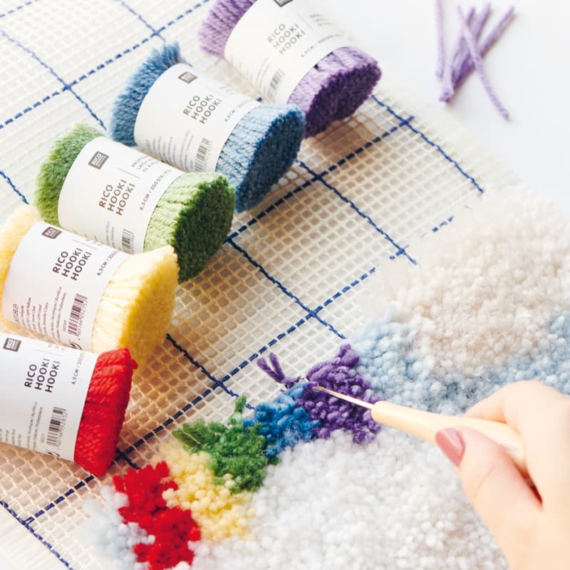 Knüpfgarn in Regebongen-Farben liegen neben geknüpftem Wandbehang