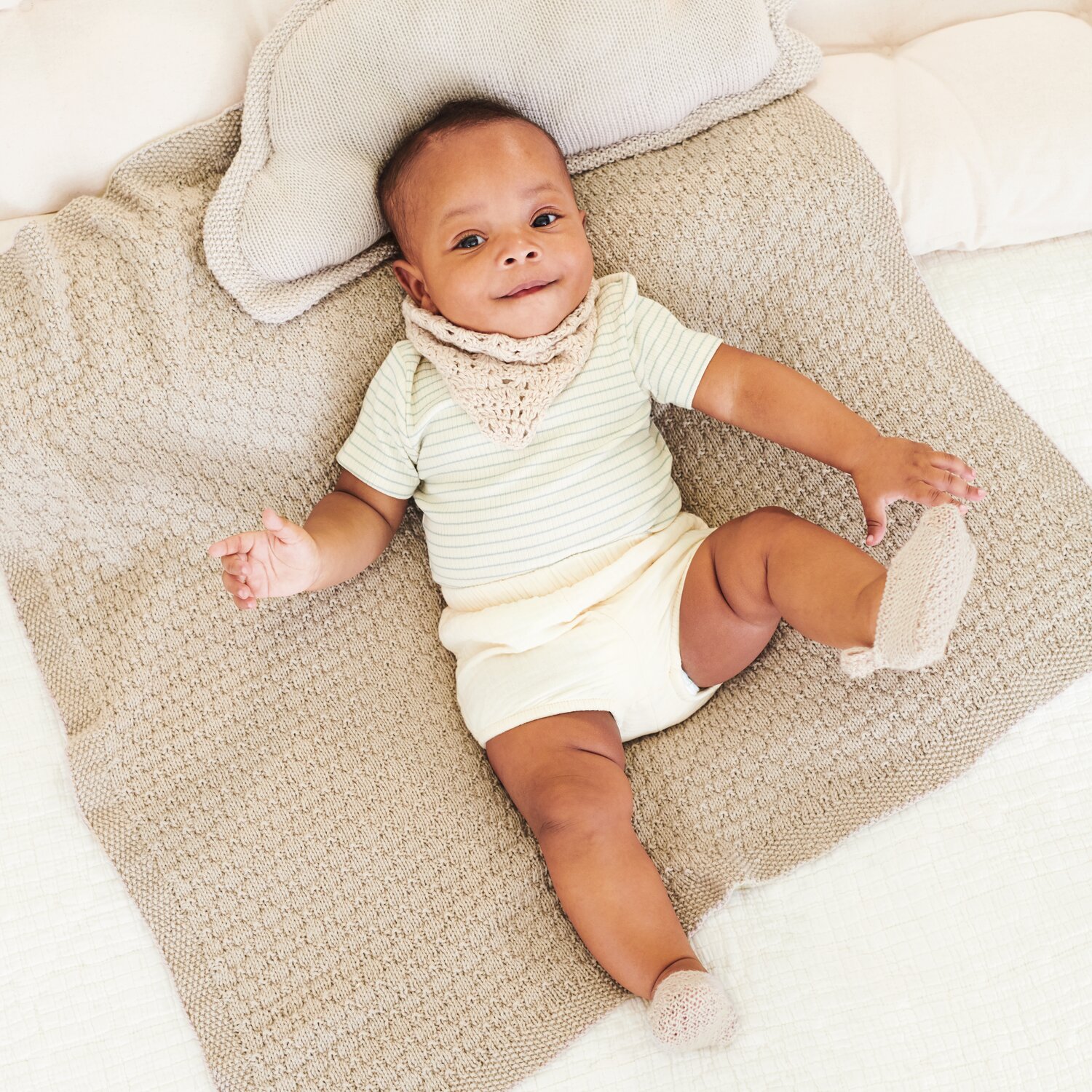 Strickset Decke Modell 02 aus Baby 043: Baby auf beiger Strickdecke mit passendem Kissen und gestrickten Accessoires.